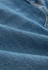 Denimsko platno u srednje plavoj nijansi, s mekom teksturom i suptilnim varijacijama u debljini, te horizontalnim uzorkom tkanja.