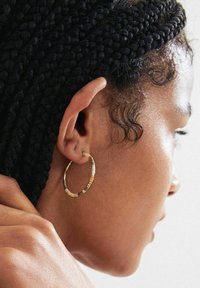 Gold hoop earrings with multicolored beads in green, beige, and white. Close-up view highlighting texture and shape against skin.