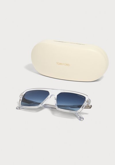 Lunettes de soleil rectangulaires Tom Ford à monture transparente avec verres bleu foncé, posées à côté d'un étui crème marqué Tom Ford.