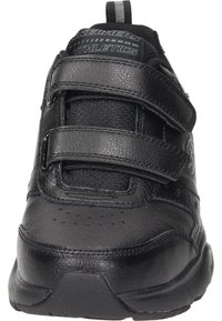 Scarpa sportiva nera con tomaia in pelle sintetica, doppi cinturini in velcro, punta arrotondata, dettagli perforati sulla punta e suola imbottita.