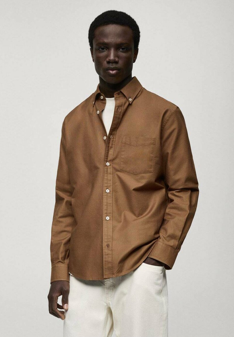 Brown button-up shirt with a single chest pocket, made of textured fabric, paired with light-colored trousers.