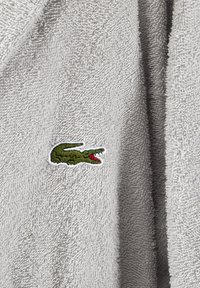 Accappatoio in spugna grigia con una texture morbida, caratterizzato da un piccolo logo di coccodrillo ricamato in verde.