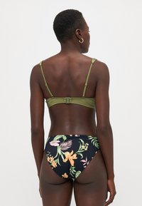 Bikini-set med en olivengrønn topp med justerbare stropper og en svart bunn som viser livlige blomster mønstre. Glatt stofftekstur.