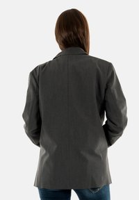 Blazer gris ajustado con una textura suave, hombros estructurados y una abertura trasera sencilla. Presenta una solapa notch clásica y líneas limpias.