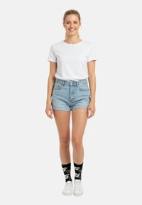 Vit kortärmad t-shirt kombinerad med ljusblå denimshorts. Svarta strumpor med blommönster och vita sneakers fulländar stilen.