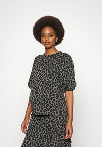 Blusa de maternidade e saia em padrão de leopardo escuro, com mangas bufantes, tecido suave e um ajuste confortável na cintura.
