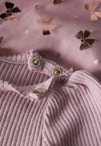 Tissu rose clair ornée de motifs de papillons en rose doré brillant ; texture côtelée avec des boutons assortis en haut.