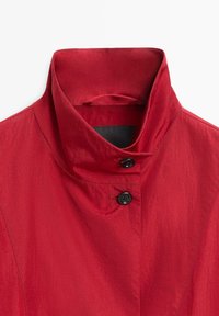 Rote Jacke mit hohem Kragen, zwei schwarzen Knöpfen vorne und einem strukturierten Stoff mit leicht zerknittertem Aussehen.