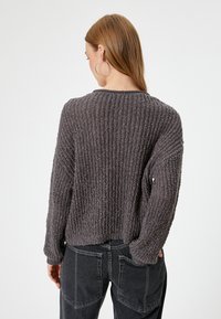 Donkergrijze gebreide trui met een textuur van ribbelstructuur, boxy vorm en brede mouwen. Voorzien van een ronde halslijn en een ontspannen pasvorm.