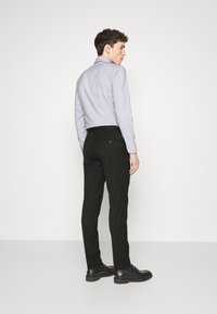 Camicia a righe lilla, con colletto alla francese, abbinata a pantaloni neri aderenti e scarpe nere, vista da dietro.