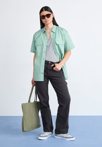 Cămașă mint verde cu mânecă scurtă, cu două buzunare frontale, top gri fără mâneci, pantaloni cu dungi, adidași gri și albi, și geantă tote verde măsliniu.