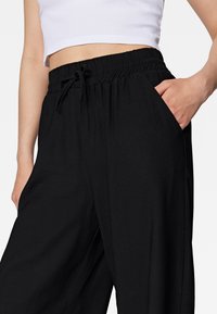 Black elastic waistband pants with a drawstring, featuring side pockets and a smooth texture, intended for comfort and ease of movement.