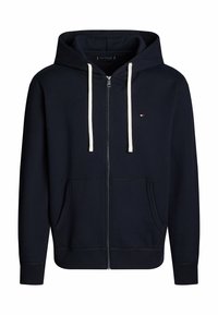 Sweat à capuche zippé bleu marine en tissu doux, avec une capuche à cordon, deux poches avant et un petit détail logo sur la poitrine.
