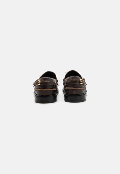 Mocasines de cuero marrón con un acabado suave, que presentan un detalle de doble hebilla, un tacón negro bajo y una punta redondeada.