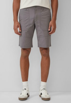 Shorts cargo gris en tissu léger, dotés de deux poches latérales, de panneaux couturés et d'une coupe droite. Associés à des baskets blanches.