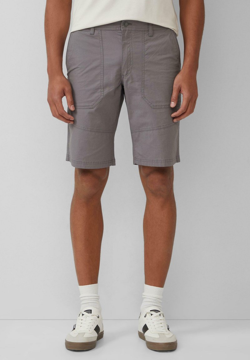 Shorts cargo gris en tissu léger, dotés de deux poches latérales, de panneaux couturés et d'une coupe droite. Associés à des baskets blanches.