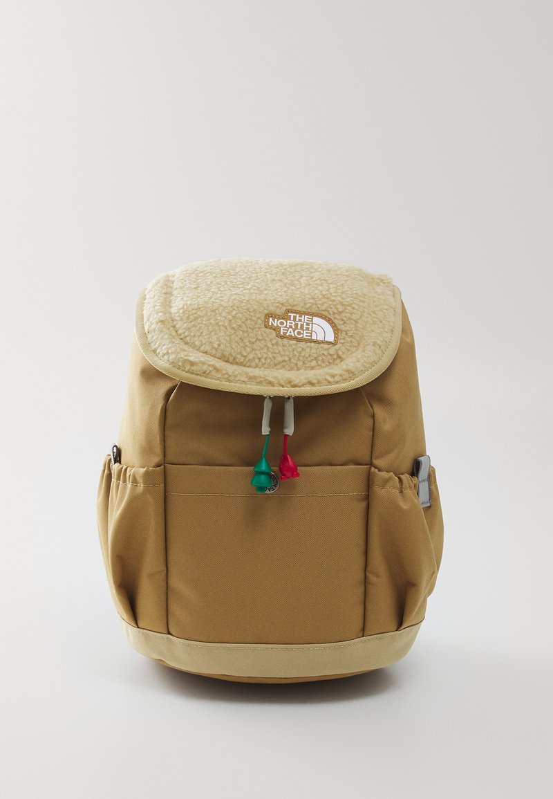 Κίτρινο σακίδιο με έναν φουντωτό κρεμ χρωματιστό καπάκι, προσαρμόσιμες πλευρικές τσέπες και πολυχρωματικές λαβές φερμουάρ. Το λογότυπο της μάρκας είναι ορατό στο καπάκι.