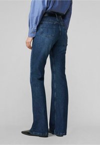 Blaue Jeans mit Schlag, die eine glatte Textur, ein Fünf-Taschen-Design und dezente Ausbleichungen aufweisen. Ergänzt durch einen schwarzen Gürtel und dunkle Schuhe.