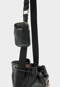 Zwarte leren emmer tas met een gestructureerde schouderband en gouden hardware. Voorzien van een kleine ritssluiting pouch die aan de schouderband is bevestigd.
