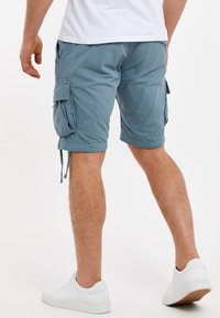 Shorts cargo blu realizzati in tessuto leggero, con tasche laterali e orli con cordoncino, abbinati a sneakers bianche su uno sfondo neutro.