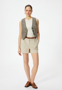 Beige shorts yhdistettynä musta-valkoiseen ruudulliseen liiviin, kevyeseen hihattomaan puseroon alla ja ruskeisiin loafereihin, luoden raikkaan ja hyvin yhdistelemän asun.