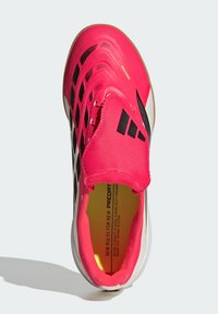 Φωτεινό ροζ ποδοσφαιρικό παπούτσι με μαύρα γεωμετρικά σχέδια, μαύρο λογότυπο τριών ρίγων και κίτρινο κείμενο στην εσωτερική σόλα, σε θέα από πάνω.