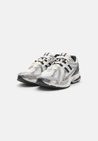 Laufschuhe mit einem Obermaterial aus weißem und silbernem Netzgewebe, schwarzen Akzenten, dicken Schnürsenkeln und einer strukturierten schwarzen Gummisohle.