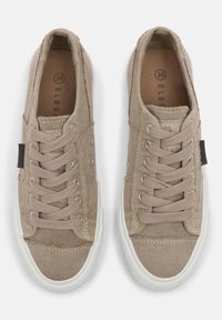 Beige Segeltuch-Sneaker mit weißer Gummisohle, Schnürdesign mit Metallösen und einem Stoffetikett an der Seite. Größe 38 ist innen markiert.