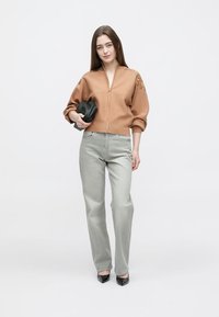Tan lynlås-sweater med puffede ærmer, parret med lysegrå jeans med lige ben. Modellen holder en sort clutch og står foran en hvid baggrund.