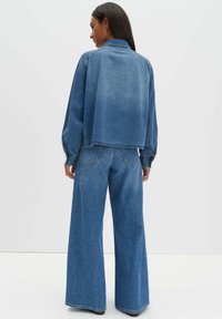 Jeansjacke mit kurzem Design, Ballonärmeln und ausgebleichter blauer Farbe, kombiniert mit weit geschnittenen blauen Jeans mit klassischem Schnitt.