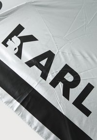 Ezüst esernyő fényes felülettel, nagy fekete betűkkel "KARL" felirattal, és fekete díszítéssel az alsó szélen.