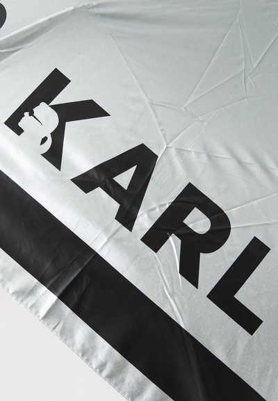 Parapluie argenté avec une finition brillante, arborant un grand texte noir inscrivant "KARL", et un accent noir le long du bord inférieur.