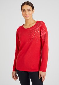 Rode trui met lange mouwen en een ronde halslijn, versierd met een patroon van zilveren rhinestones aan één zij. Zacht, gestructureerd stof.
