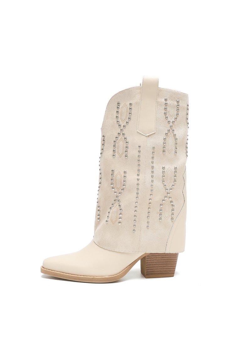 Botas de vaquero beige con punta afilada, parte superior de ante, tachuelas decorativas plateadas en un patrón de hoja y un tacón de madera apilada.