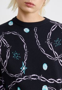 Sweater preto com padrões abstratos multicoloridos, apresentando círculos azuis e desenhos em rosa claro. Gola redonda canelada e textura macia.