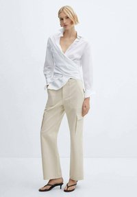 White wrap shirt with a pointed collar, paired with beige wide-leg cargo pants featuring side pockets. Worn with black strappy sandals.