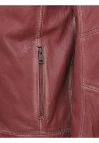 Rode leren jas met zichtbare ritsdetails op de linkerarm, gestructureerd oppervlak en gestikte accenten langs de naden.