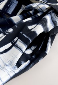 Tissu au motif abstrait en noir et blanc avec des plis doux, montrant des textures superposées et des ombres sur une surface claire.