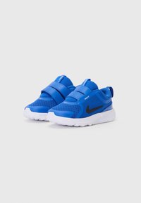 Chaussures de sport en mesh bleu avec deux bandes Velcro, semelle blanche et accent logo noir. Design à bout rond avec un matériau supérieur respirant.