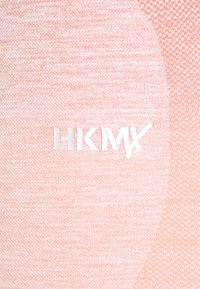 Ljusrosa tyg med en texturerad mönstring; pryds av den vita logotypen "HKMX" i en modern typsnitt, placerad centralt.