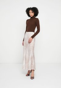 Ruda, aptempta golfas su ilgėjančia, lengva šviesiai smėlio spalvos suknele, kurioje subtilus gyvūnų raštas. Juodi basutės su dirželiais.