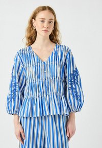 Blå och vit randig blus med V-ringning, puffärmar och broderade detaljer på ämarna, med en rynkad midja och knappar.