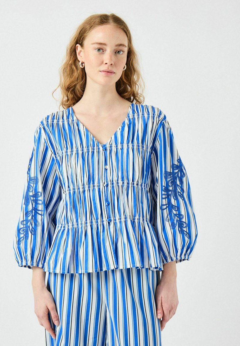 Blå och vit randig blus med V-ringning, puffärmar och broderade detaljer på ämarna, med en rynkad midja och knappar.