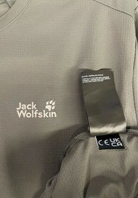 Vêtement gris Jack Wolfskin avec logo de marque visible, étiquette d'entretien et étiquettes de certification CE UKCA sur tissu texturé.
