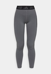 Leggings sportivi grigi con una ampia vita nera che presenta un logo del marchio. Texture liscia, design aderente e tasche laterali per riporre gli oggetti.