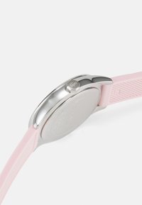 Montre ronde avec un boîtier en acier inoxydable argenté, un bracelet en silicone rose et des accents texturés. Comprend une couronne avec un logo et un dos lisse.