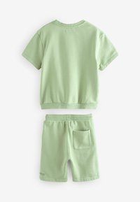 Lys grøn bomulds t-shirt og shorts sæt. T-shirten har korte ærmer og en rund halsudskæring, shortsene har elastisk talje og sidelomme.