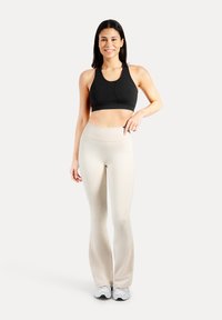 Zwarte sportbeha met een ronde hals, gecombineerd met lichtbeige flared leggings. Beide gemaakt van rekbare, zachte stof. Witte sneakers maken de outfit compleet.