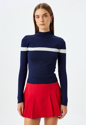Navy ribbed long-sleeve top with a white horizontal stripe, paired with a red pleated mini skirt. The outfit features a fitted design and soft texture.