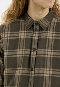 Bruine en beige geruite shirt met een knoopsluiting kraag, voorzien van zwarte knopen en een zachte, gestructureerde stof.